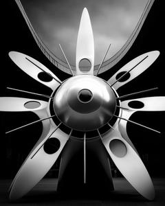 Airplane propeller from below, surrounded by dramatic sky and city buildings.