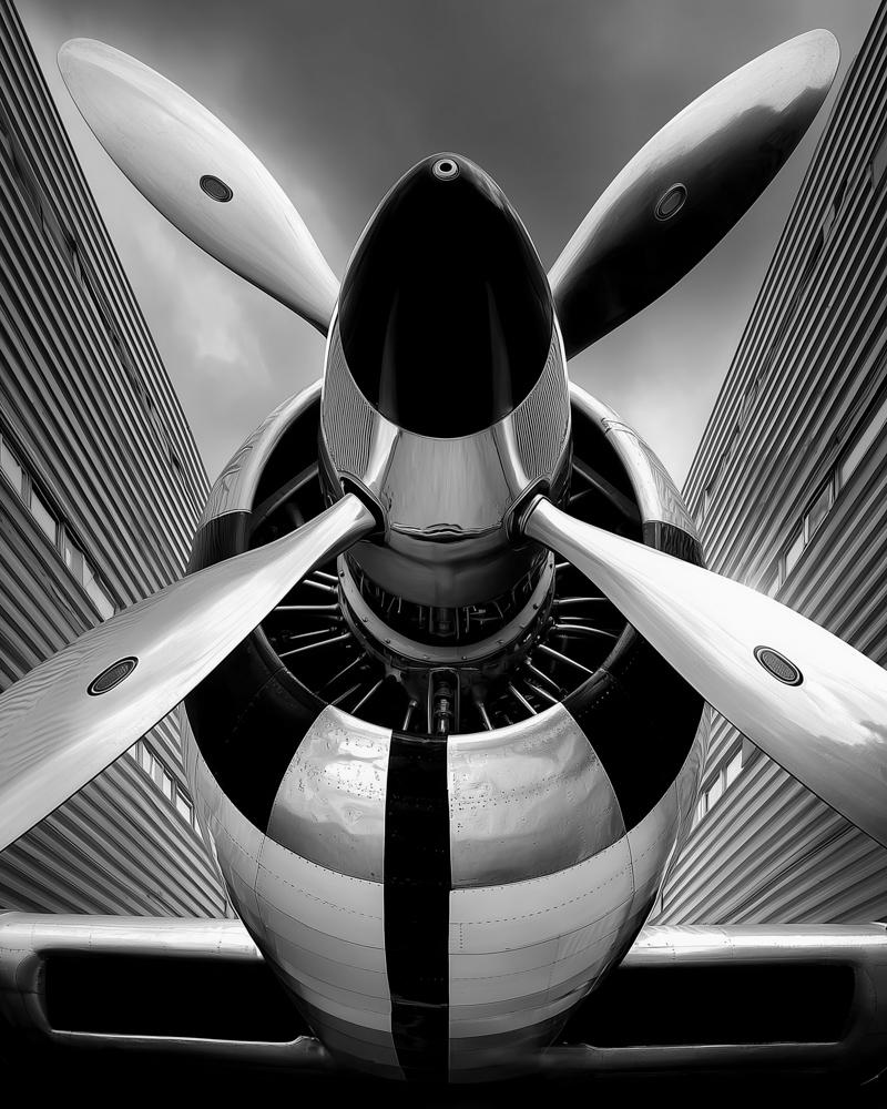 Front view of a sleek airplane propeller, framed by tall modern buildings.